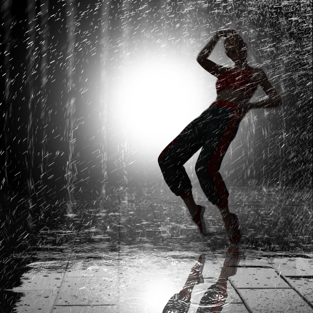 Silhuetten av en person som danser i regn med en sterk lyskaster bak seg.