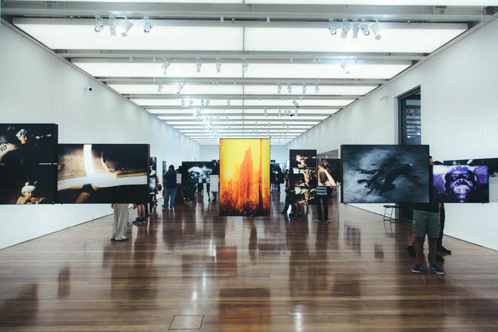 Folk går blant kunstneriske bilder på en utstilling.