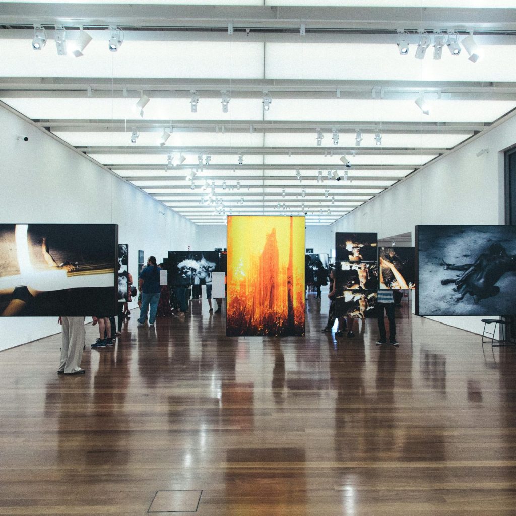 Folk går blant kunstneriske bilder på en utstilling.
